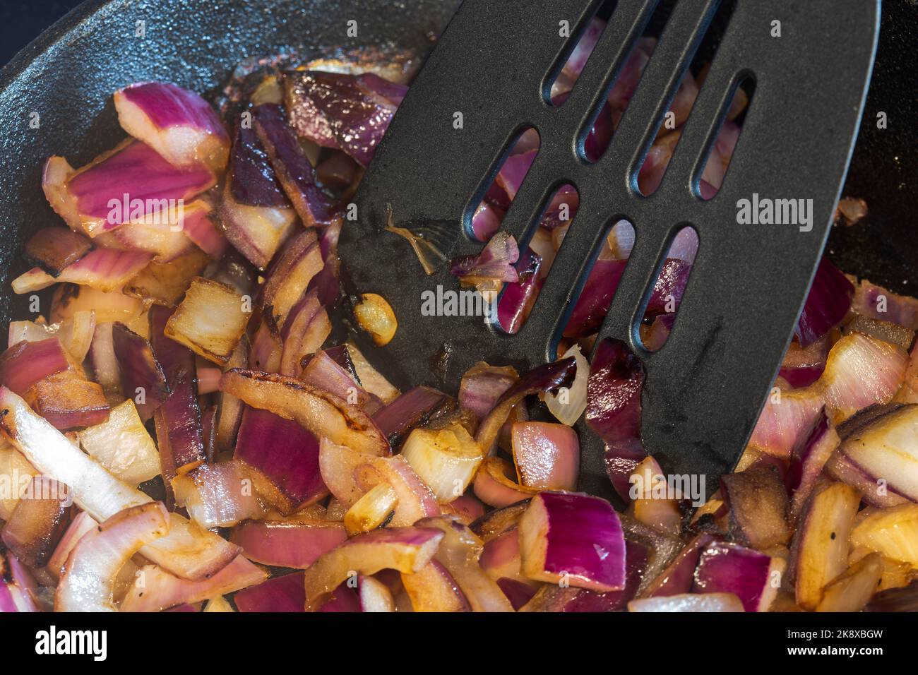 Frying red onions, with olive oil, in a cast iron frying pan, on an electric hob stove. Stock Photo
