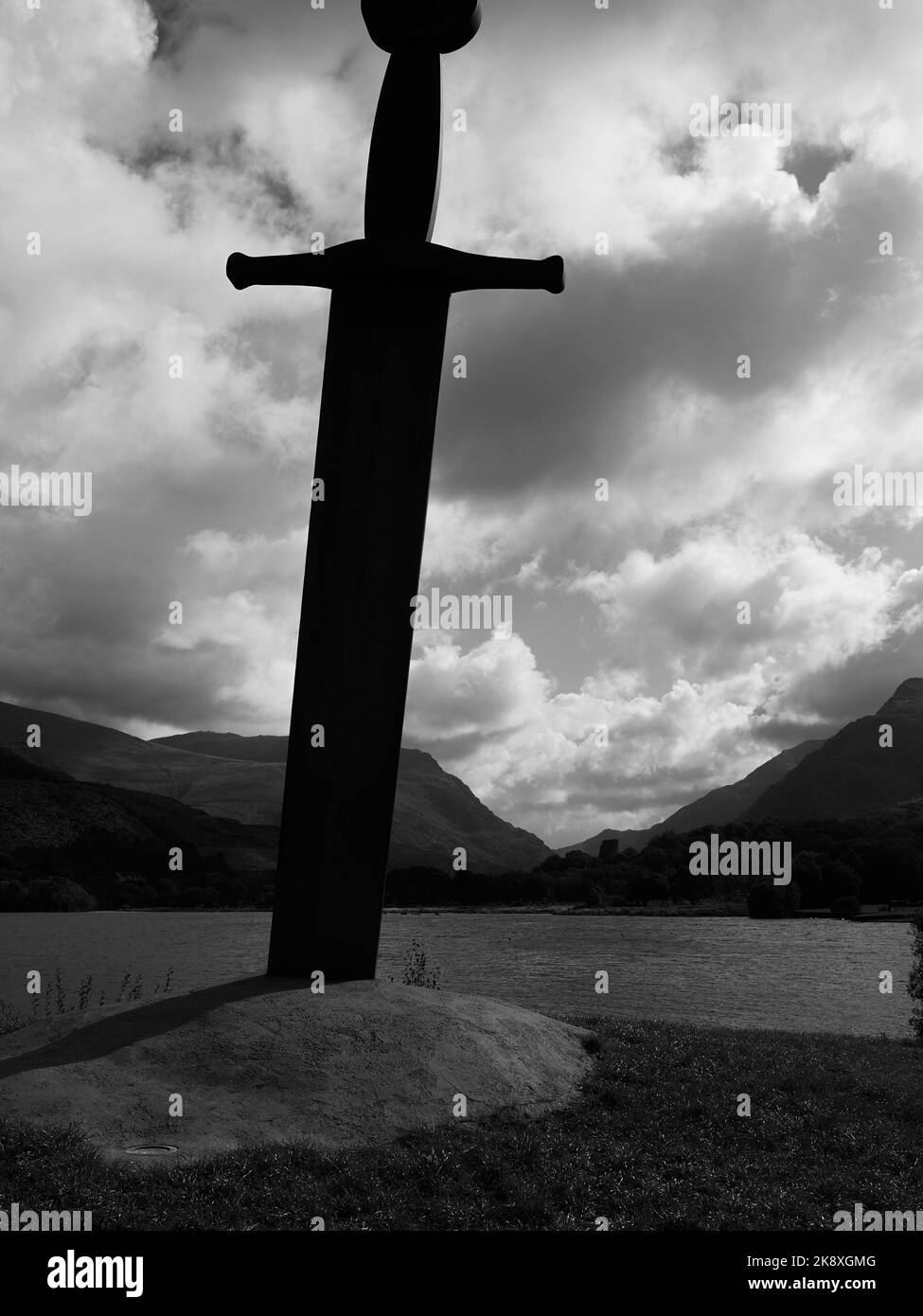 A vertical grayscale shot of a sword monument on the shore of Llynnau Mymbyr lake in Wales Stock Photo