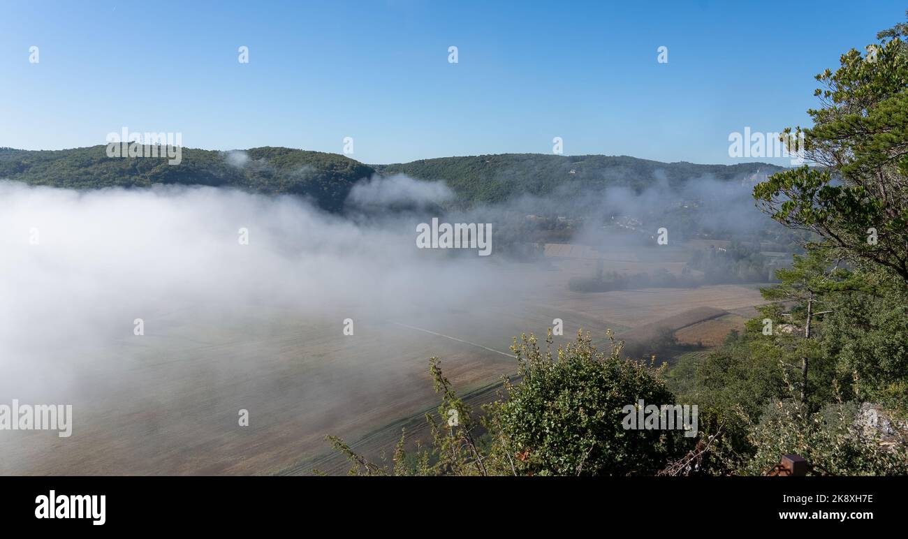 looking down through morning mist in to a valley with agricultural patterned fields, distant hills and clear blue sky Stock Photo