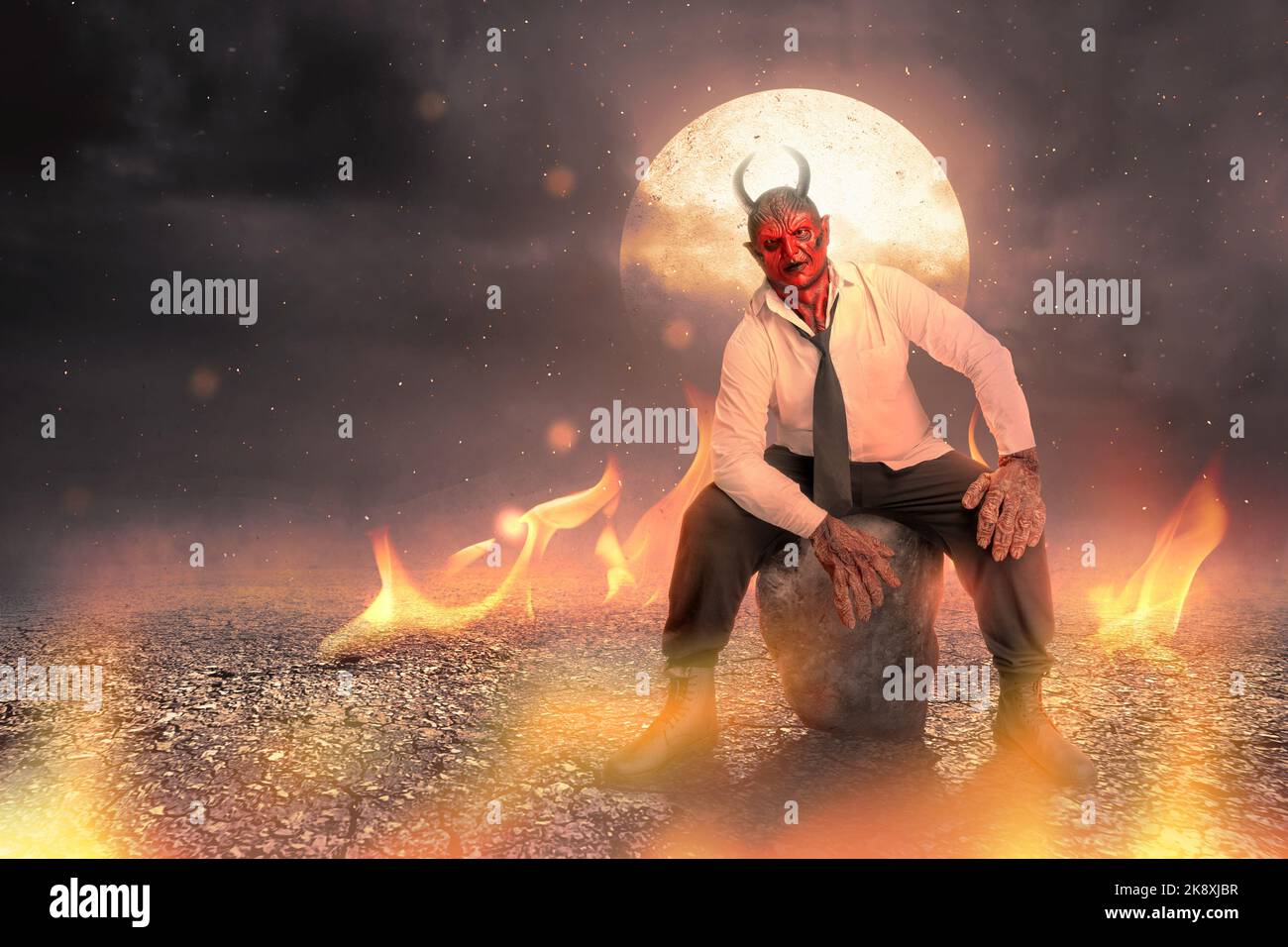 Devilman is sitting with a fire and full moon background. Halloween concept Stock Photo