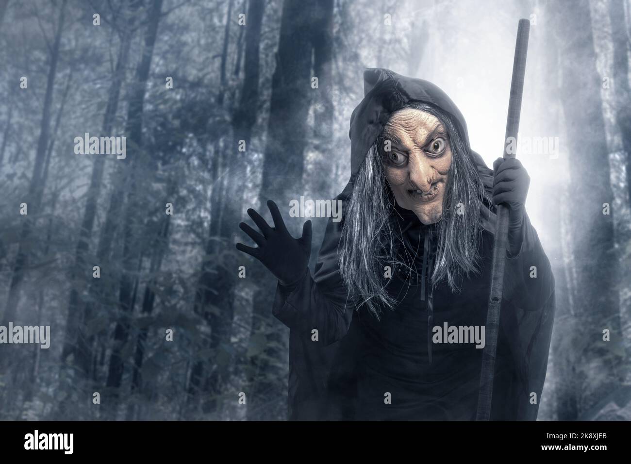 Old witch in a cloak with a stick standing in the forest with a ...