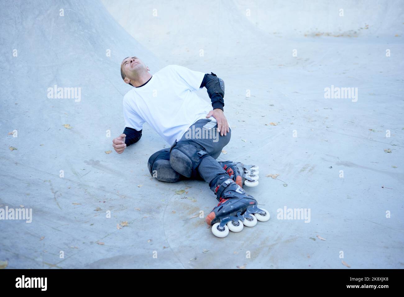Fall, leg injury. Man on roller skates lying on wooden covering track