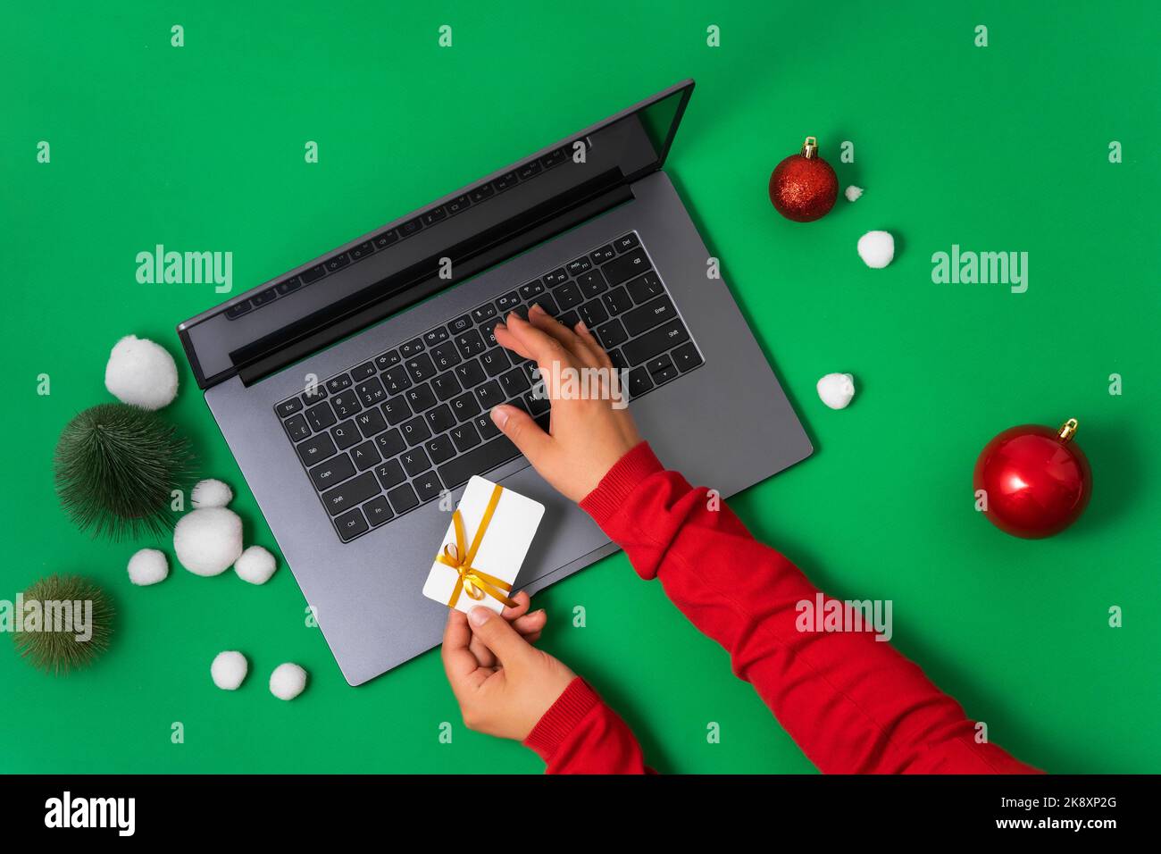 Women's hands with bank, credit card pays for online shopping on laptop. Top view of green background with Christmas decor, flat lay. The concept of C Stock Photo