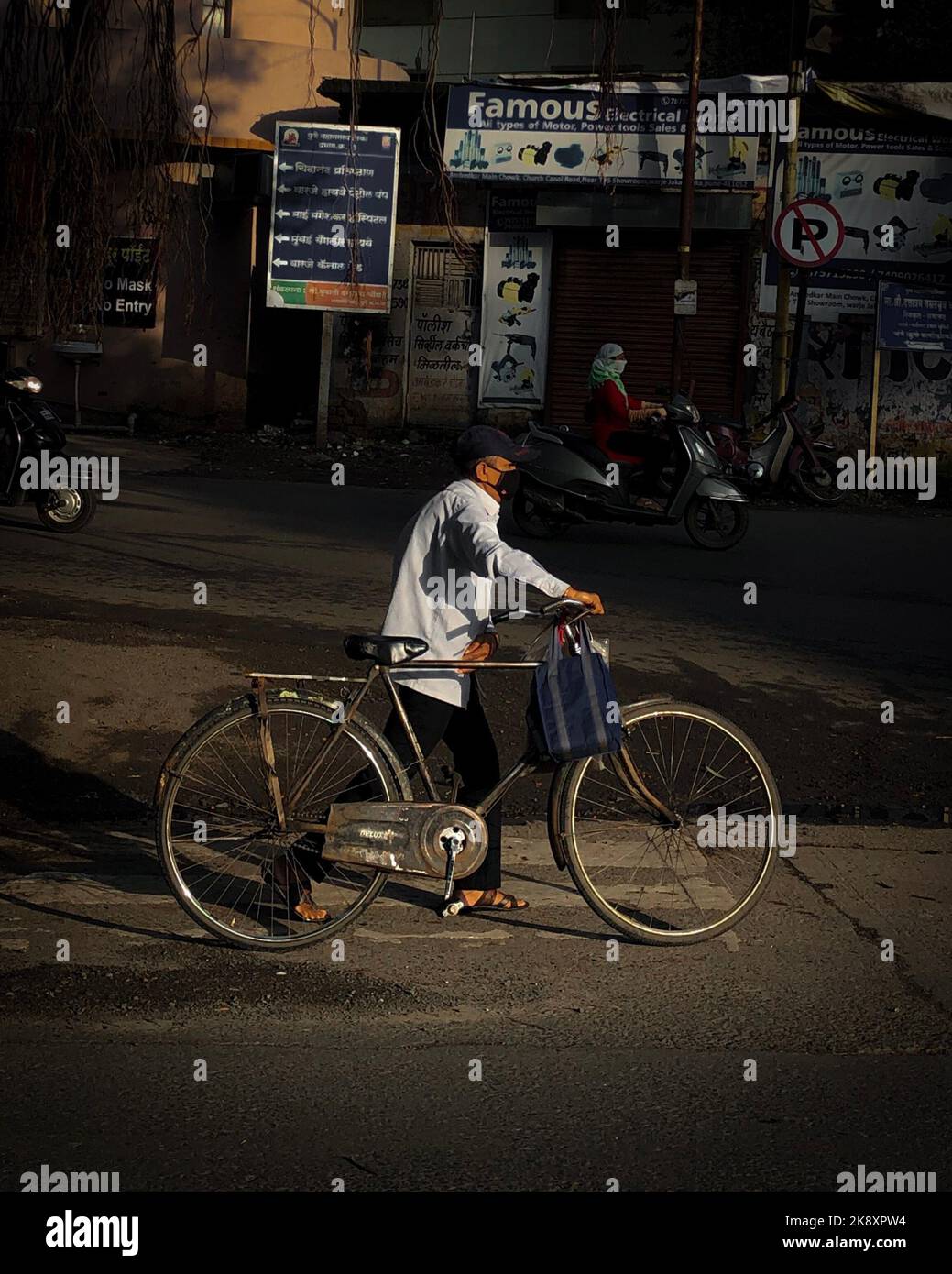 A vertical shot of a male walking while holding his bicycle in a poor district in Pune, India Stock Photo