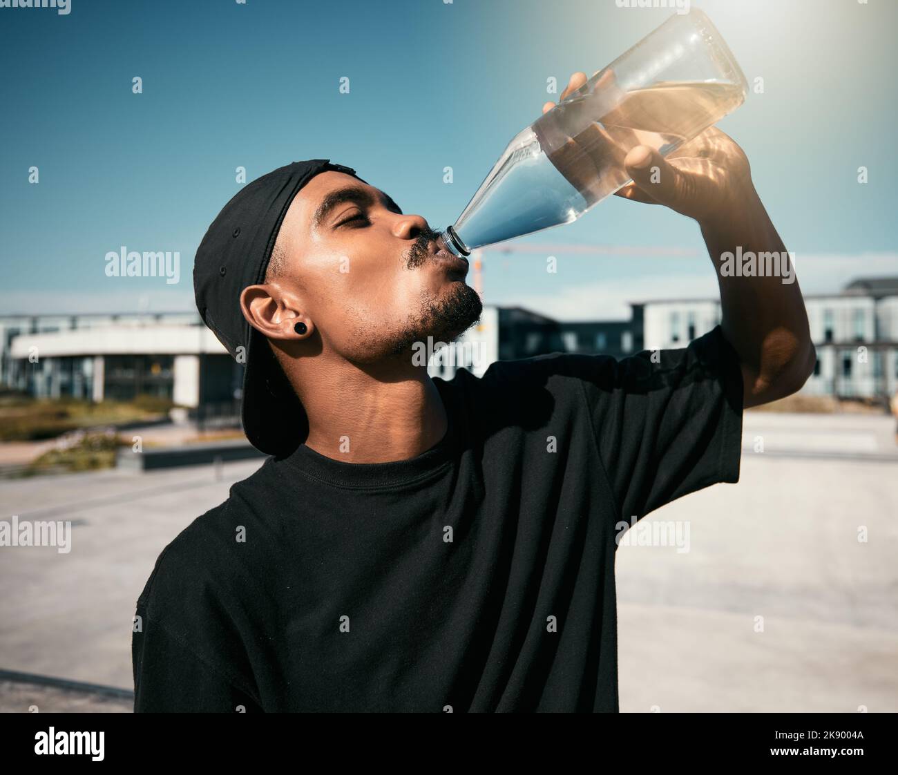 City heat, summer and black man drinking water on concrete road, thirsty gen z outdoor activity. Sun, fun and urban young man with healthy street Stock Photo