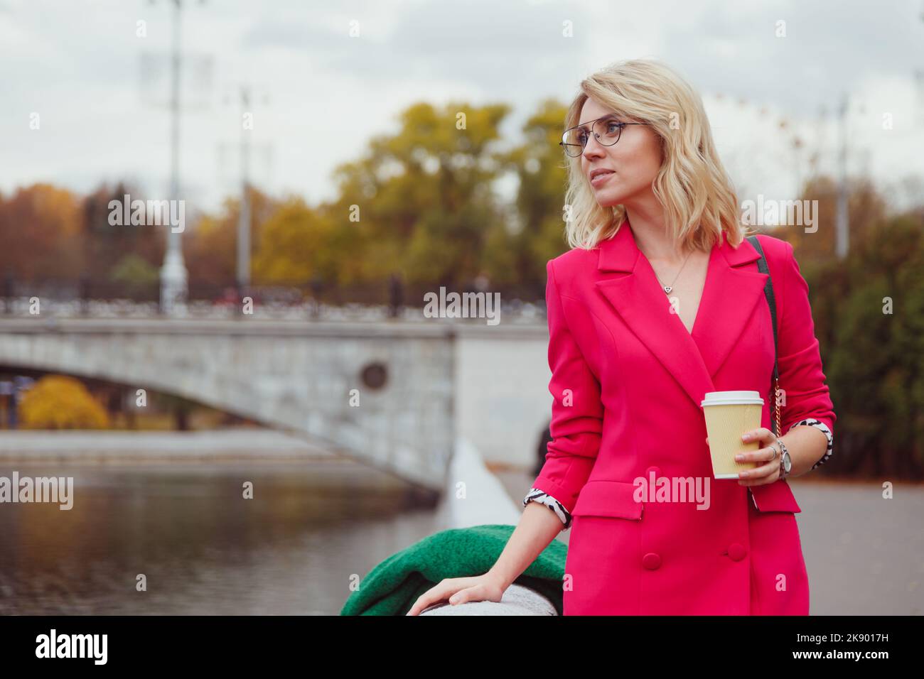 Blonde woman in pink suit drinking coffee from disposable paper cup while walking to work in