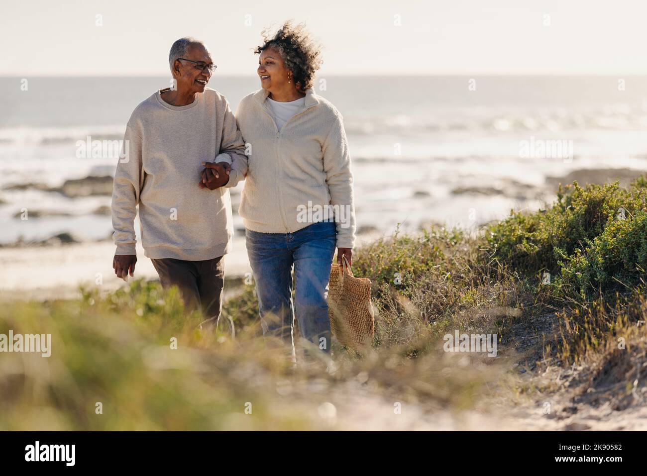 Mature couple smiling happily while walking away from the beach after a romantic picnic. Cheerful elderly couple enjoying a seaside holiday after reti Stock Photo
