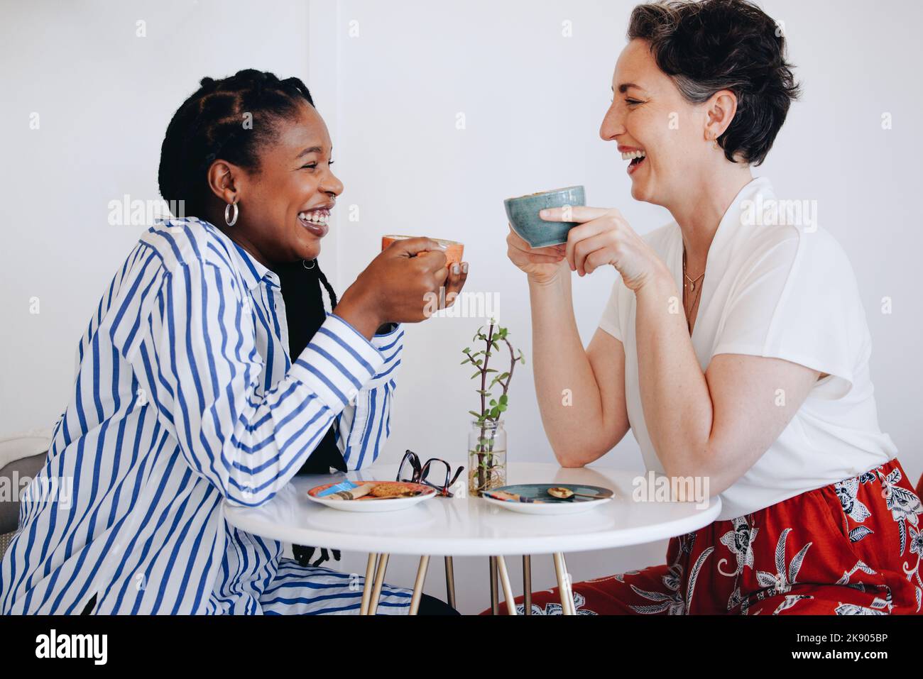 Two happy businesswomen laughing and having coffee together in an office cafe. Two cheerful business women enjoying a friendly coffee meeting in a mod Stock Photo