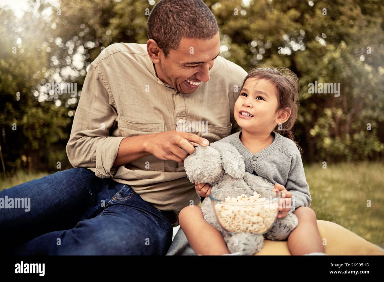 Father, girl and popcorn eating of a happy child and parent outdoor laughing with a smile. Dad, happiness and kid with food hug together with bonding Stock Photo