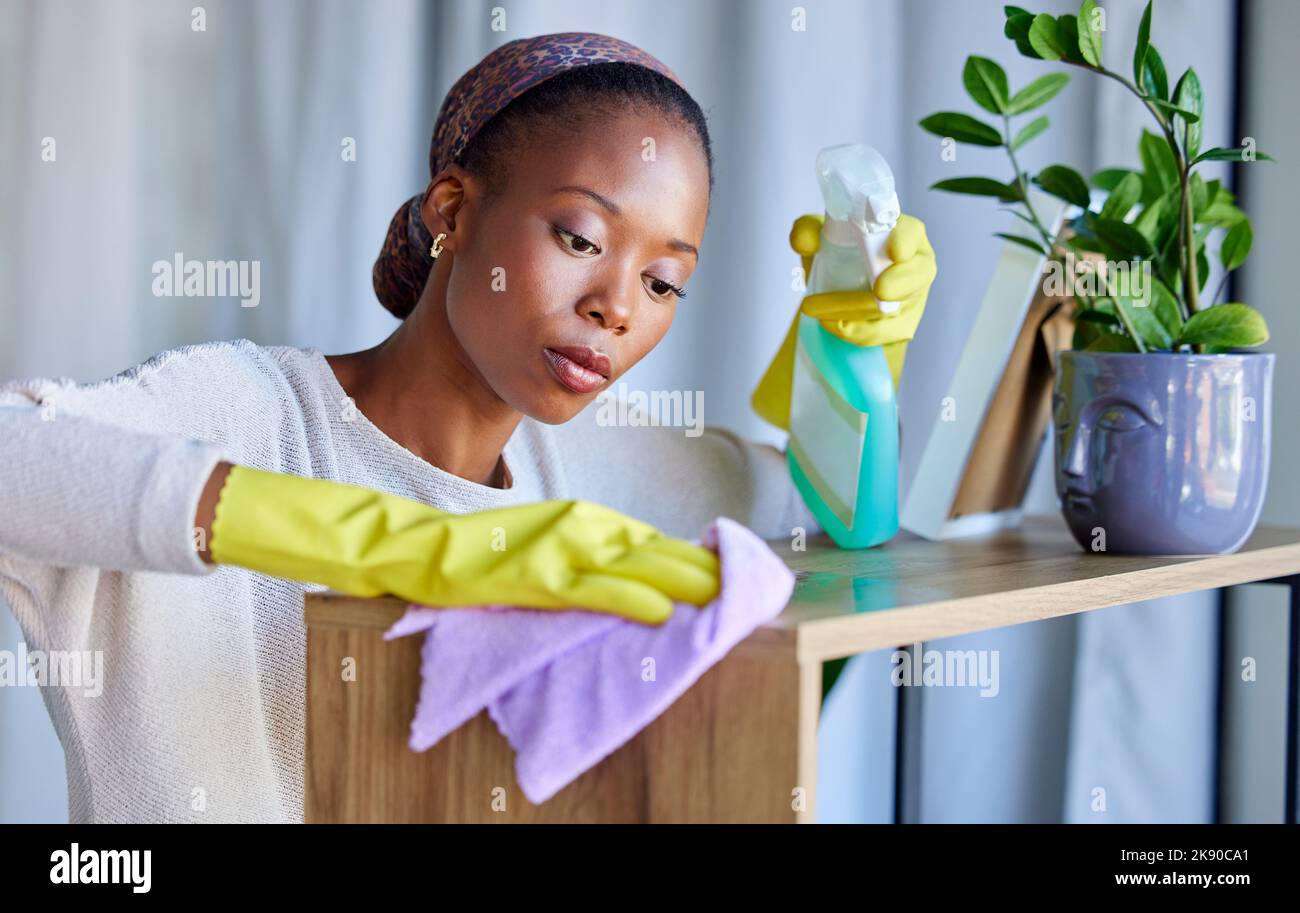 Cleaner, house and black woman cleaning dust on furniture, tables and wood with liquid soap in spray bottle and cloth. Services, maid and worker with Stock Photo
