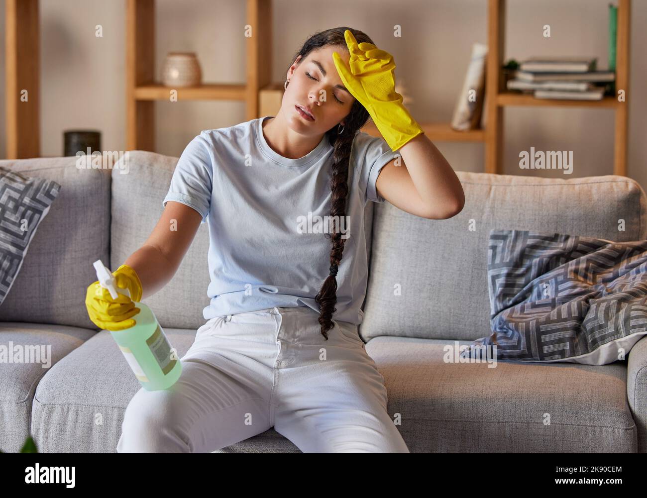 Spring cleaning, tired and sad woman headache in home living room with burnout, stress and frustrated spray task. Fatigue, pain and depression Stock Photo