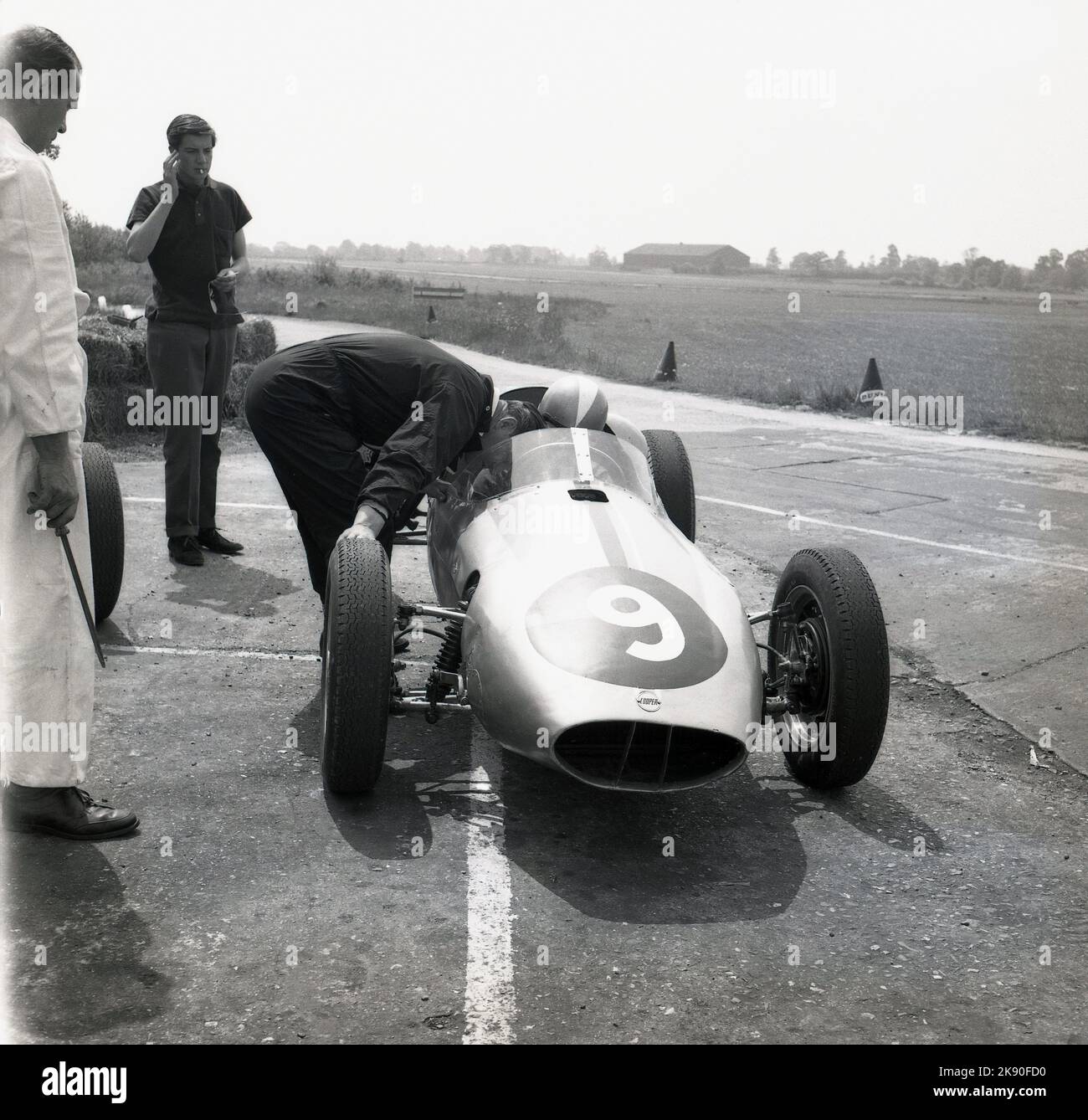 1962, historical, a man sitting in a single-seater racing car beside a track  with mechanic at Geoff Clarke’s Motor Racing Stables, a driving school based at the Finmere Aerodome, a disused RAF airfield near to Buckingham, England, UK. The racing school’s 1,000 cc single-seaters were rear-engined Formula Junior Coopers. Stock Photo