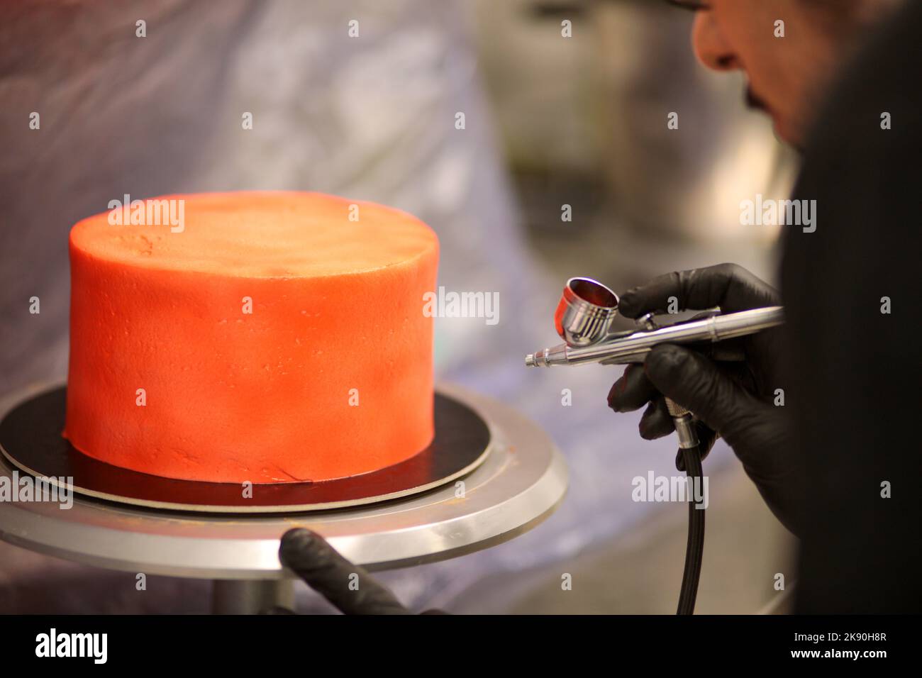 cook preparing a red frosted cake using air bush Stock Photo