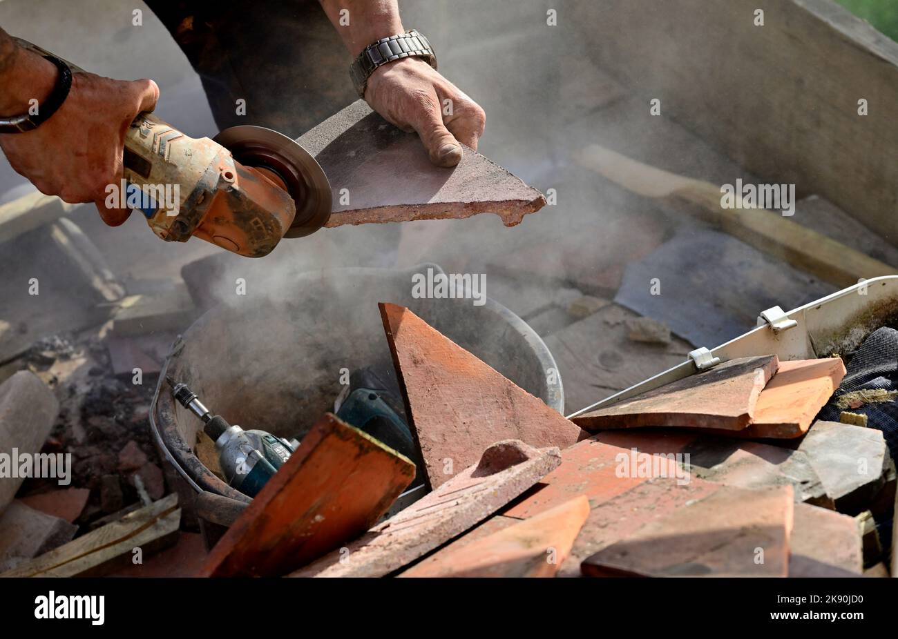 Roofing work on clay tiled residential hipped bay roof, cutting clay tile with angle grinder Stock Photo