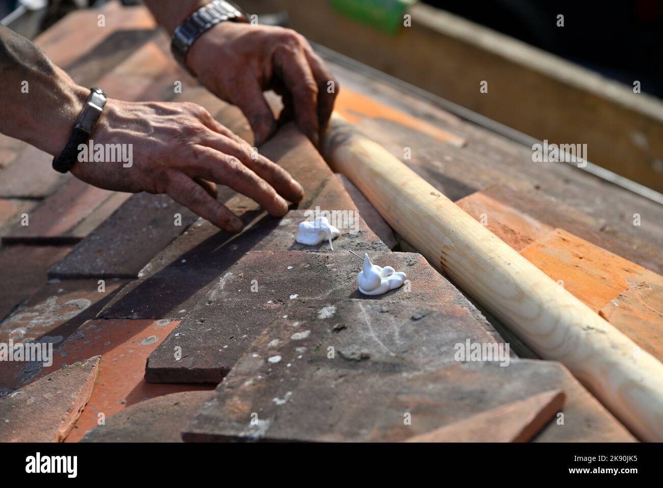 Roofing work on clay tiled residential hipped bay roof, fitting angle cut clay tiles to hip rafter Stock Photo