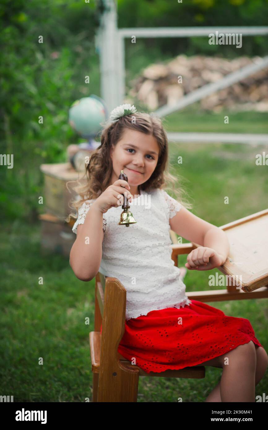 Adorable pensive schoolgirl with a bell in hand. beginning of the school year. Symbolic First Call. Learning outside the auditorium during coronavirus Stock Photo