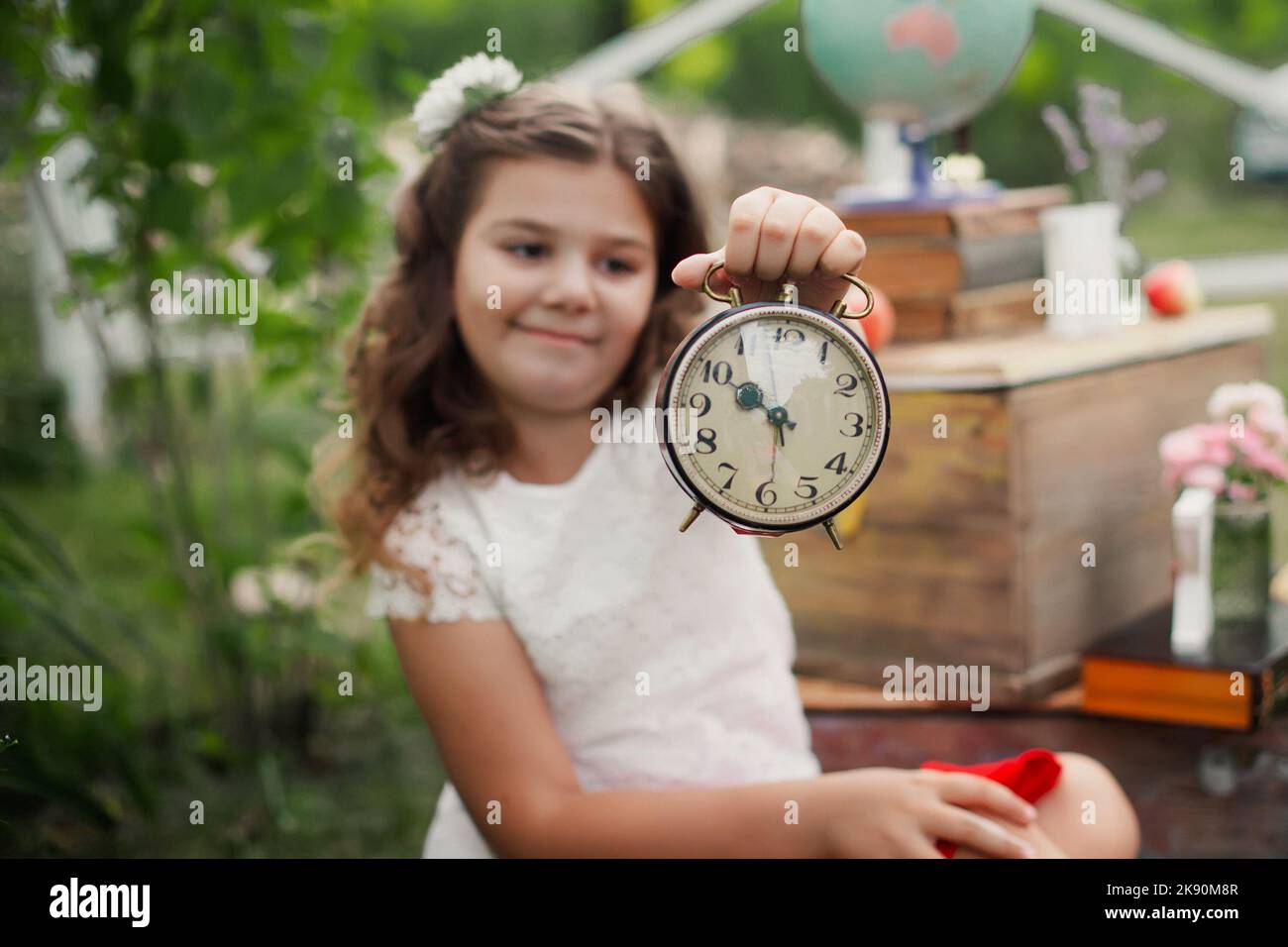 Adorable pensive schoolgirl holds an alarm clock and reports on the
