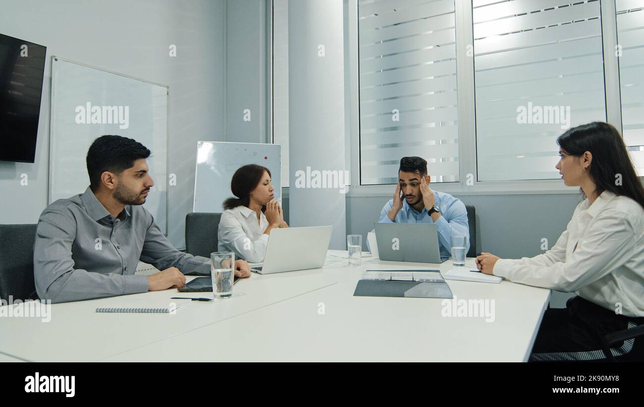Disgruntled young arab male boss scolding employees for bad work at meeting of diverse groups, angry team leader holding head reprimanding Stock Photo