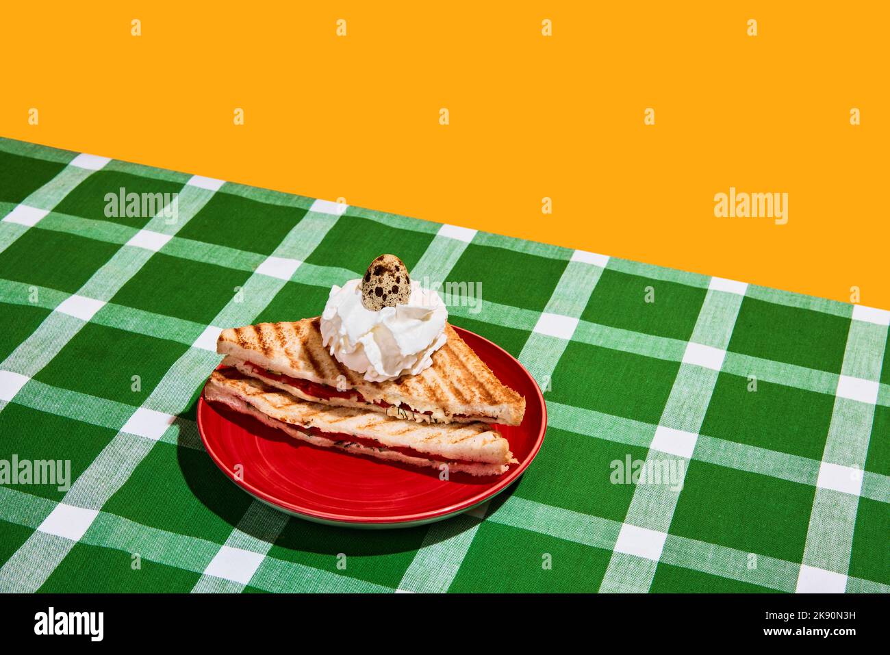 Surreal cake. Perfectionism and colorful minimalism. Meat sandwich, fried toast and raw quail egg on plaid tablecloth background. Food pop art Stock Photo