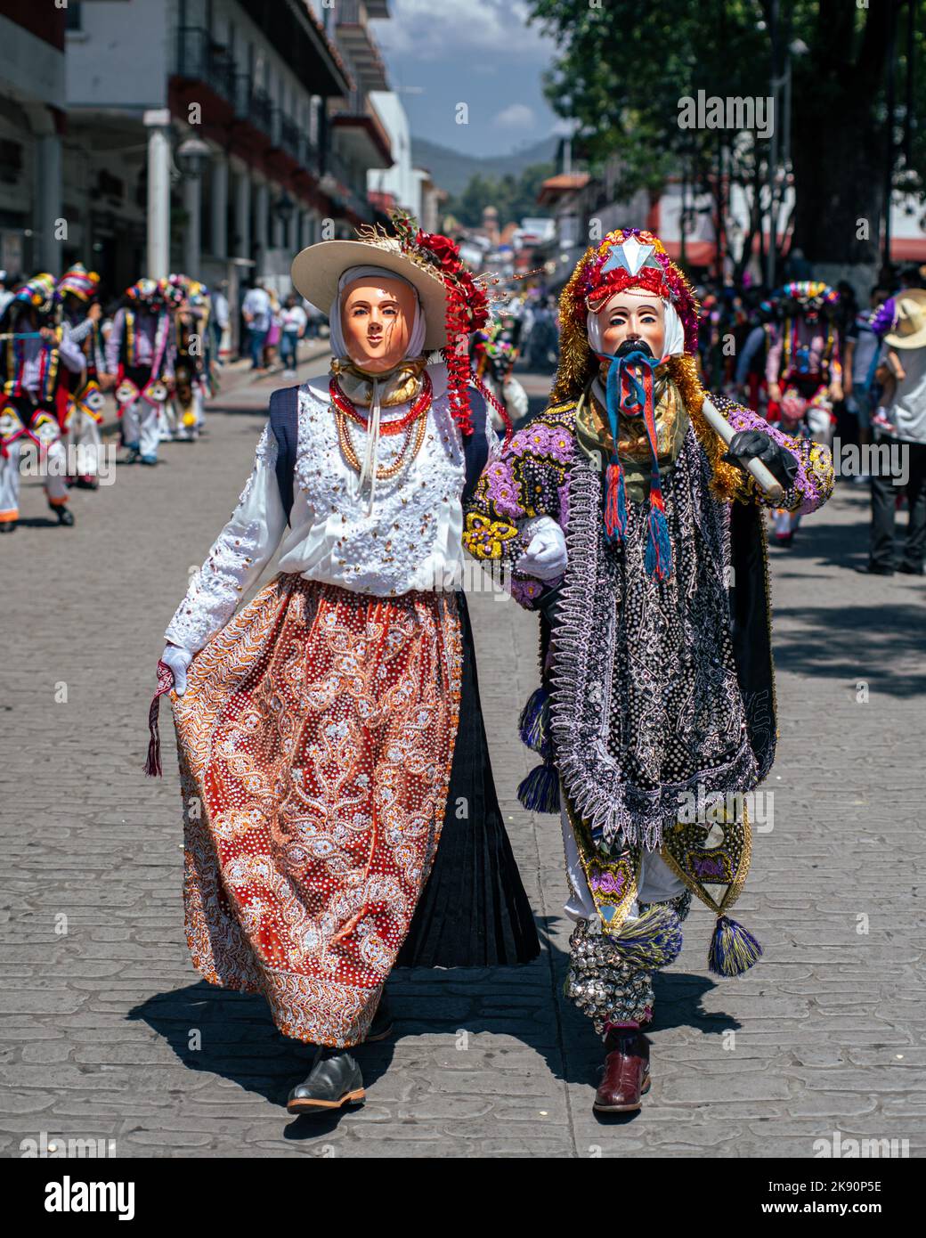 A vertical shot of a couple in traditional Mexican masks and costumes walking on the streets during a festival Stock Photo