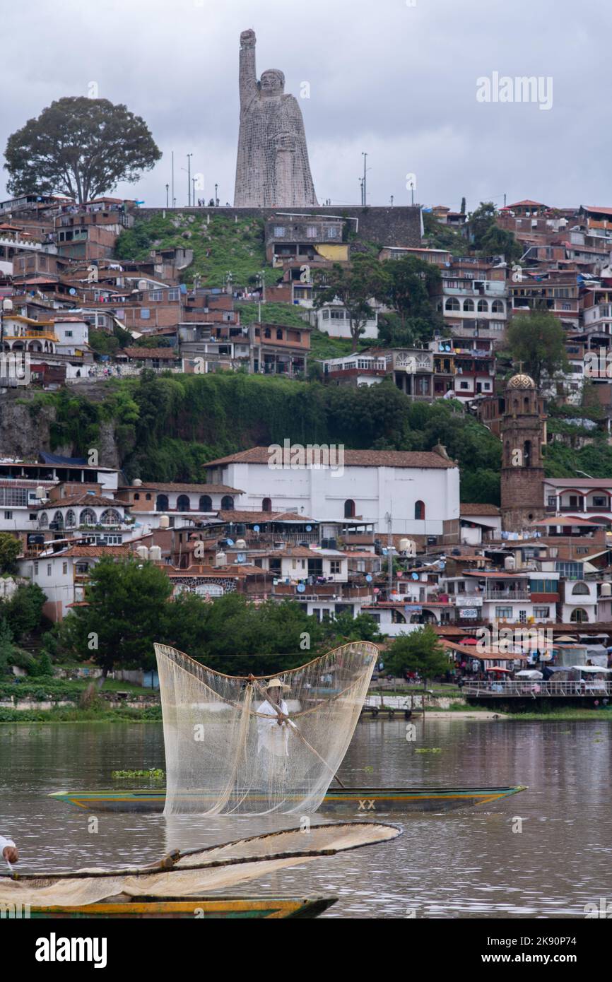 A vertical shot of a fisherman on a canoe with the Janitzio town and a big statue in the background Stock Photo