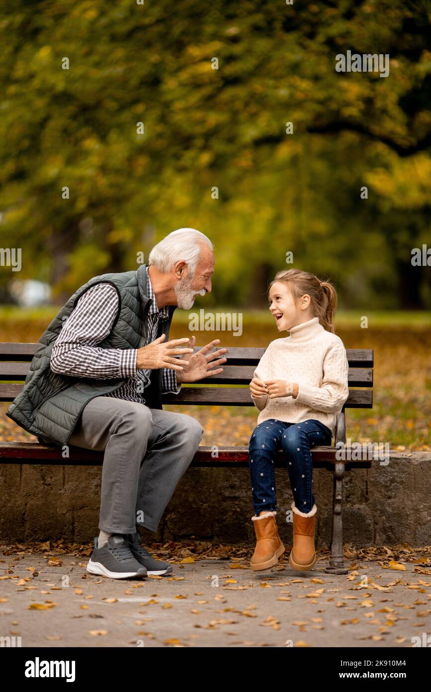 Handsome grandfather playing red hands slapping game with his granddaughter in park on autumn day Stock Photo