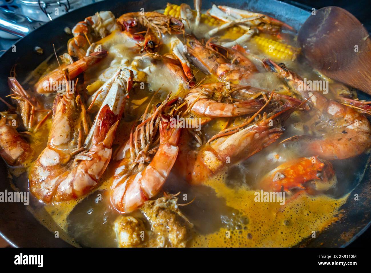 Seafood boil with crabs, prawns and corn on the cob boiling in a wok on a hob in a home kitchen. Stock Photo