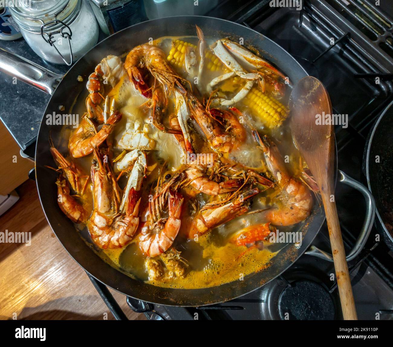 Seafood boil with crabs, prawns and corn on the cob boiling in a wok on a hob in a home kitchen. Stock Photo