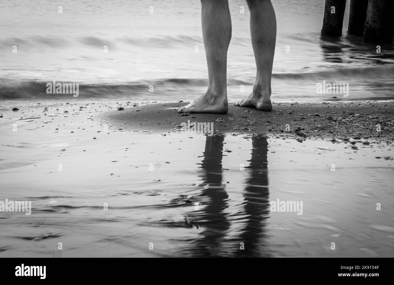A grayscale shot of human feet standing on a coastline Stock Photo - Alamy