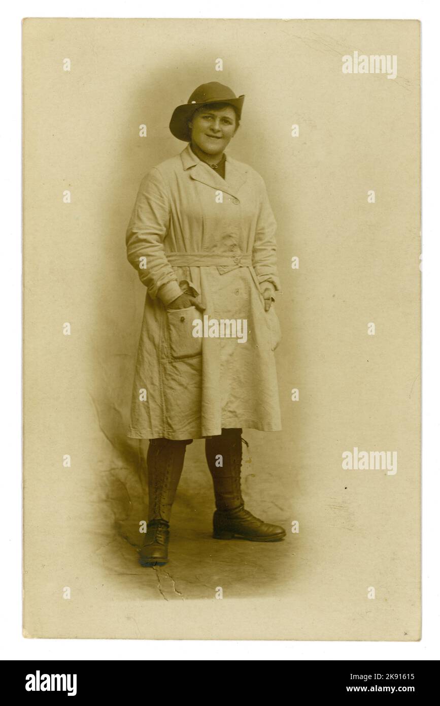 Original WW1 era studio portrait postcard of typical young Welsh Land Girl,  looking happy, wearing the standard uniform of breeches, felt hat, a knee-length overall tunic (with a button-fastening integrated belt) leather leggings and boots, U.K. dated 1918, photograph by Chapman of Swansea, Wales, U.K. Stock Photo