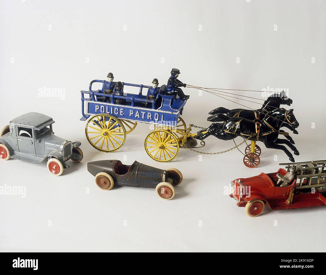 Childrens toys from the past. A cast iron toy made in USA with two horses pulling a police patrol wagon. Simple but fun toys that were cheap to buy. They are now collectible and can be very valuable. A Ford Coupe, a Alfa Romeo racing car and a firetruck in front. All cast iron toys. Stock Photo