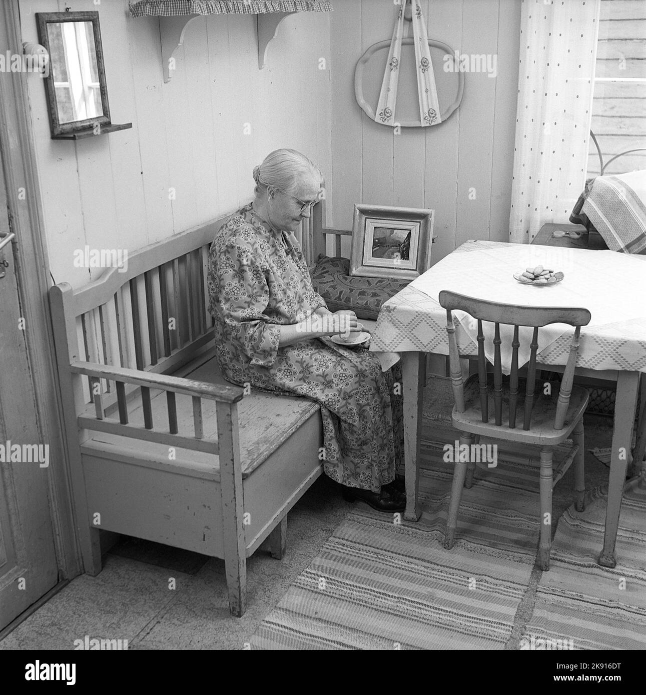 In the 1950s. An elderly lady is seen in her kitchen, sitting on a wooden sofa drinking coffee. Sweden 1953 Conard ref 2489 Stock Photo