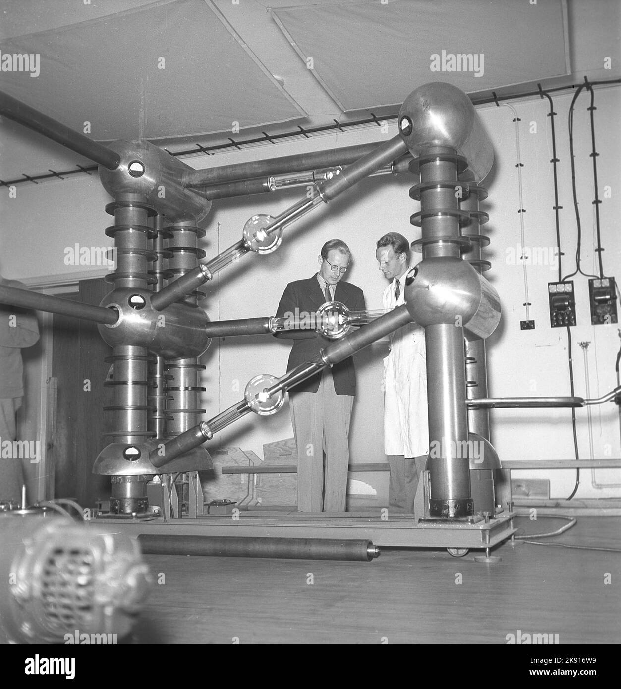 Man and machine in the 1940s. Two men are seen in a room with a unusual construction of unknown purpose. Picture taken at KTH Royal institute of Technology. Sweden 1945 Kristoffersson ref P47-3 Stock Photo