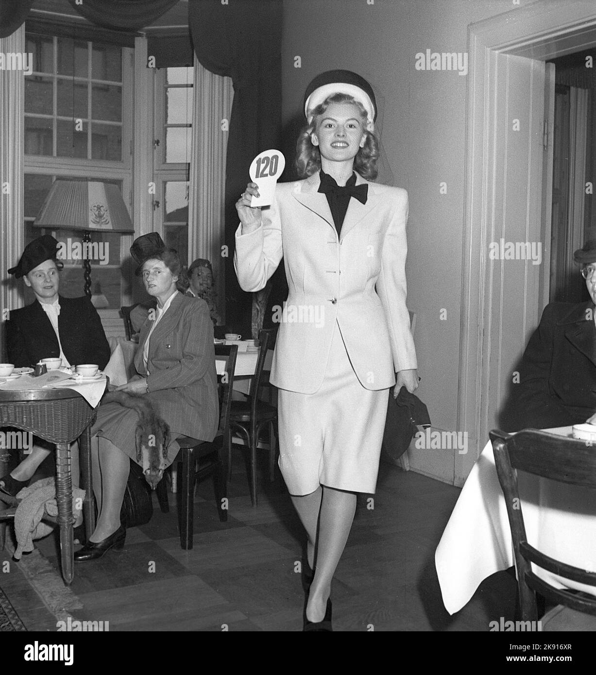 Women's fashion in the 1940s. A young woman in a 1946 outfit. A skirt with the right length, jacket, matching hat. The fashion show of ladies fashion of this year goes on in front of people in an audience. Sweden 1946  Kristoffersson T148-4 Stock Photo