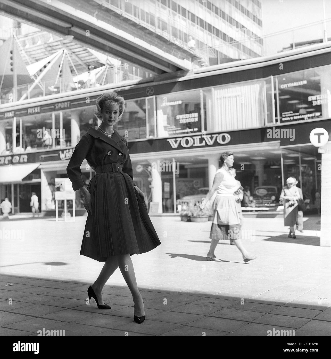 In the 1950s. A woman modelling a 1950s outfit with a jacket and skirt in matching dark. In the background a street in central Stockholm and a Volvo shop where the models Amazon and PV are on display. Sweden 1959 Kristoffersson ref CH21-9 Stock Photo
