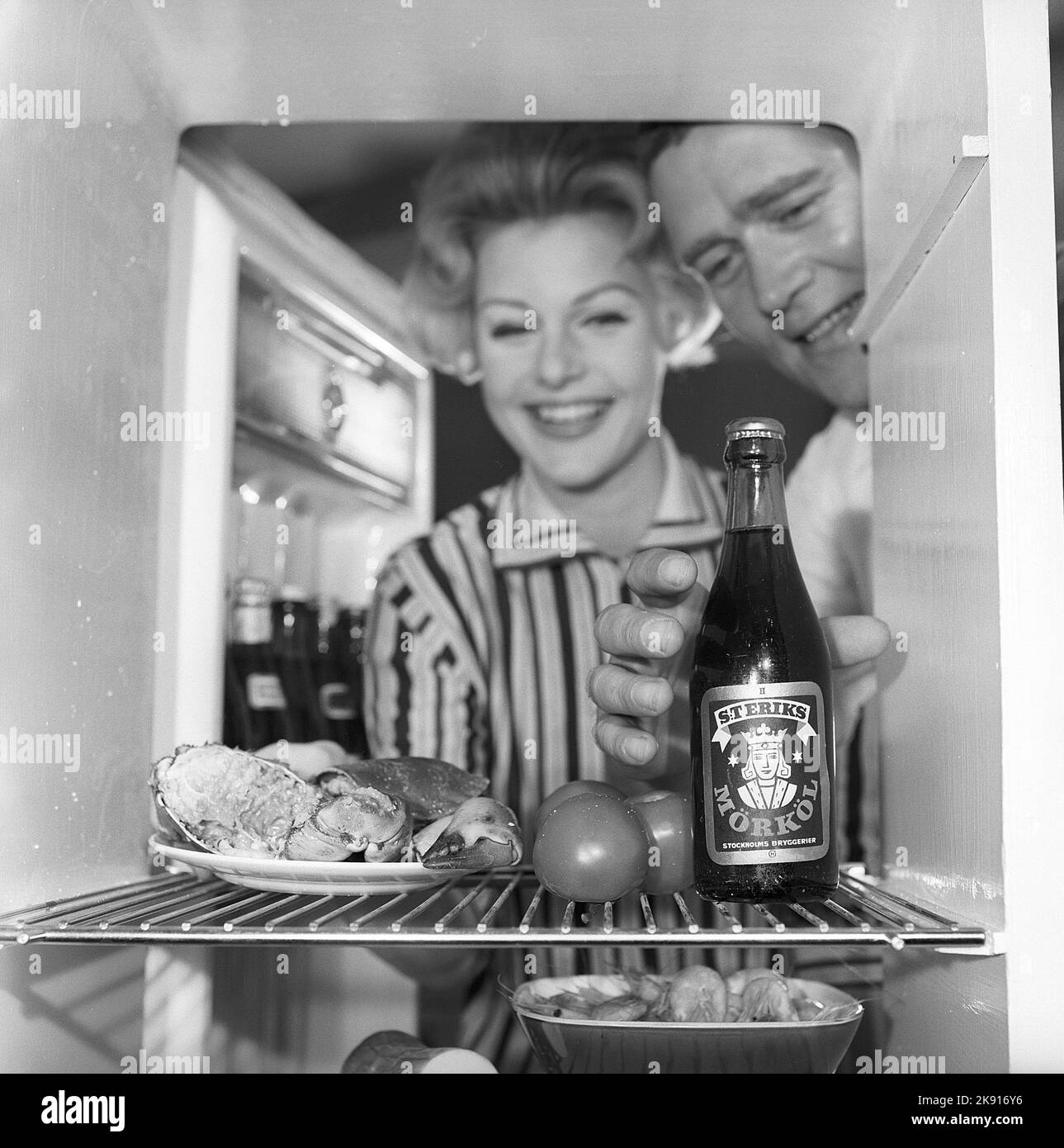 In the kitchen 1950s. A couple in their kitchen and at the refrigerator where the food and beer is kept.  Sweden 1959. Kristoffersson ref CH73-1 Stock Photo