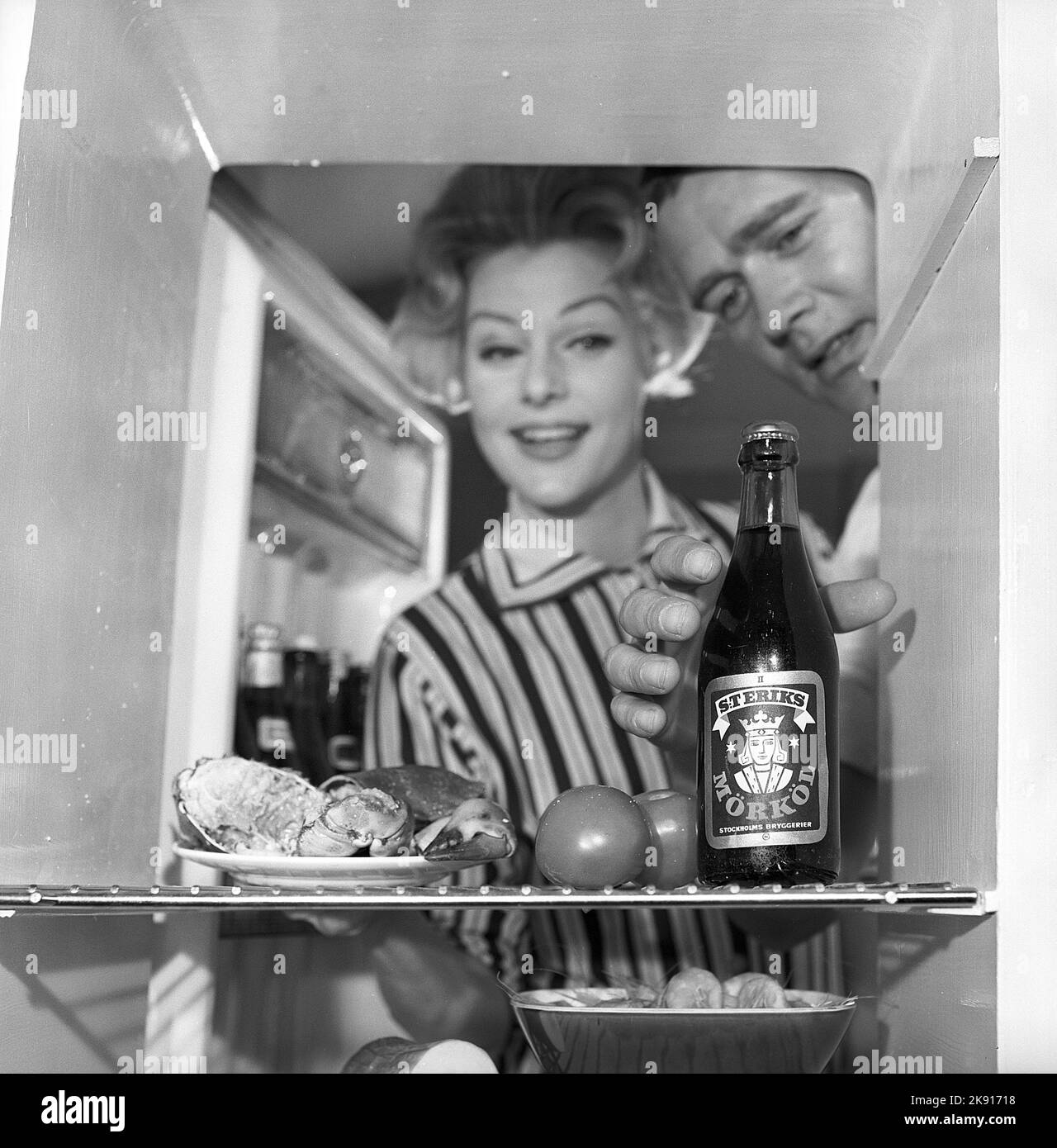 In the kitchen 1950s. A couple in their kitchen and at the refrigerator where the food and beer is kept.  Sweden 1959. Kristoffersson ref CH77-7 Stock Photo
