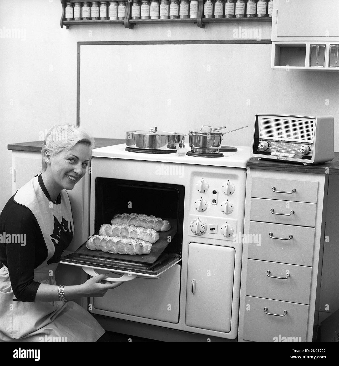 In the kitchen in the 1950s. A young woman in the kitchen taking out the ready baked breads from the oven. On top stainless steel pots and pans, a material that became popular after the aluminium era. Sweden 1959 ref Kristoffersson CQ97-6 Stock Photo