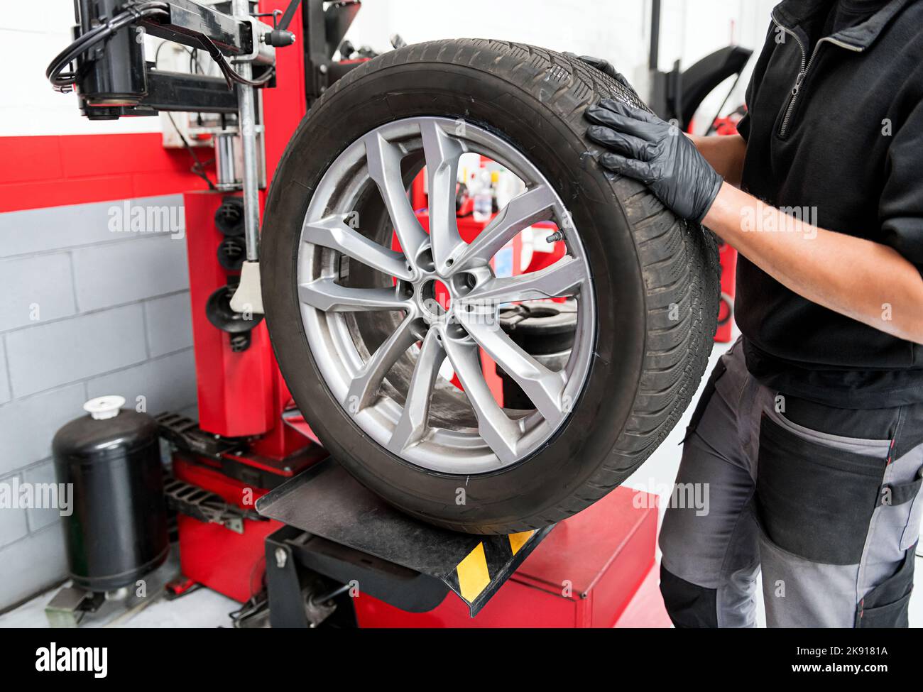 Crop servicing man in black gloves and uniform setting wheel on tire changing machine in garage workshop Stock Photo