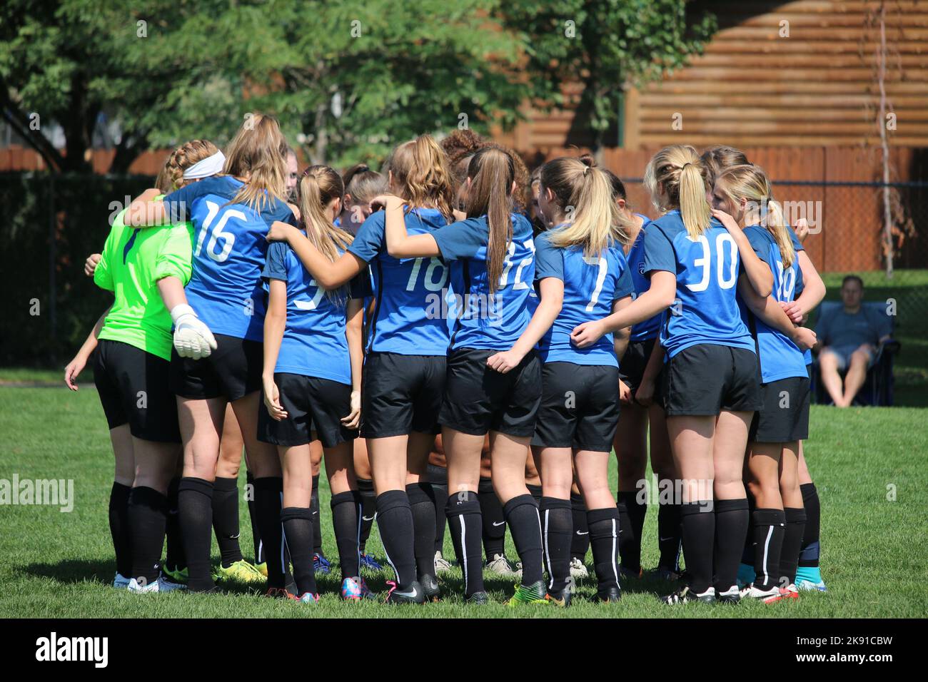 A soccer team of girls wearing blue uniform chants in a huddle Stock