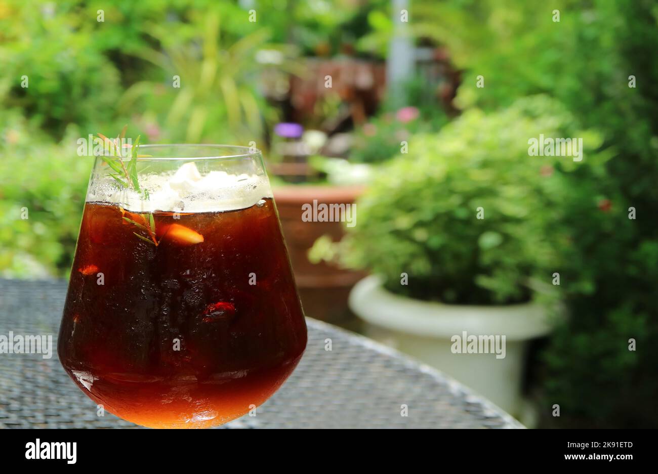 A Glass of Iced Coffee with Blurry Green Foliage in the Backdrop Stock Photo