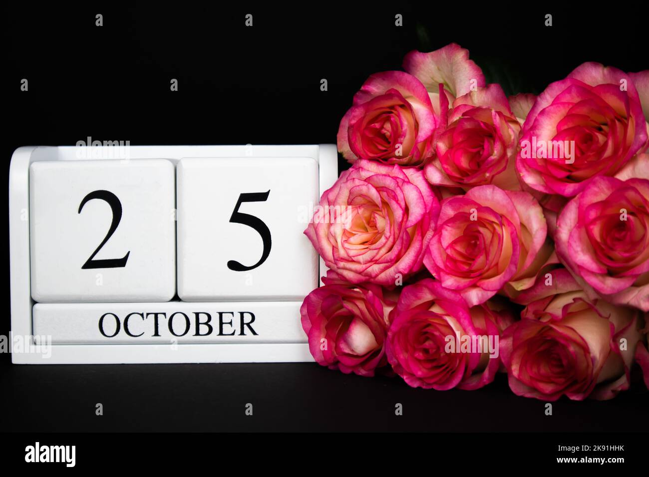 October 25 wooden calendar, white on a black background, pink roses lie nearby. Stock Photo