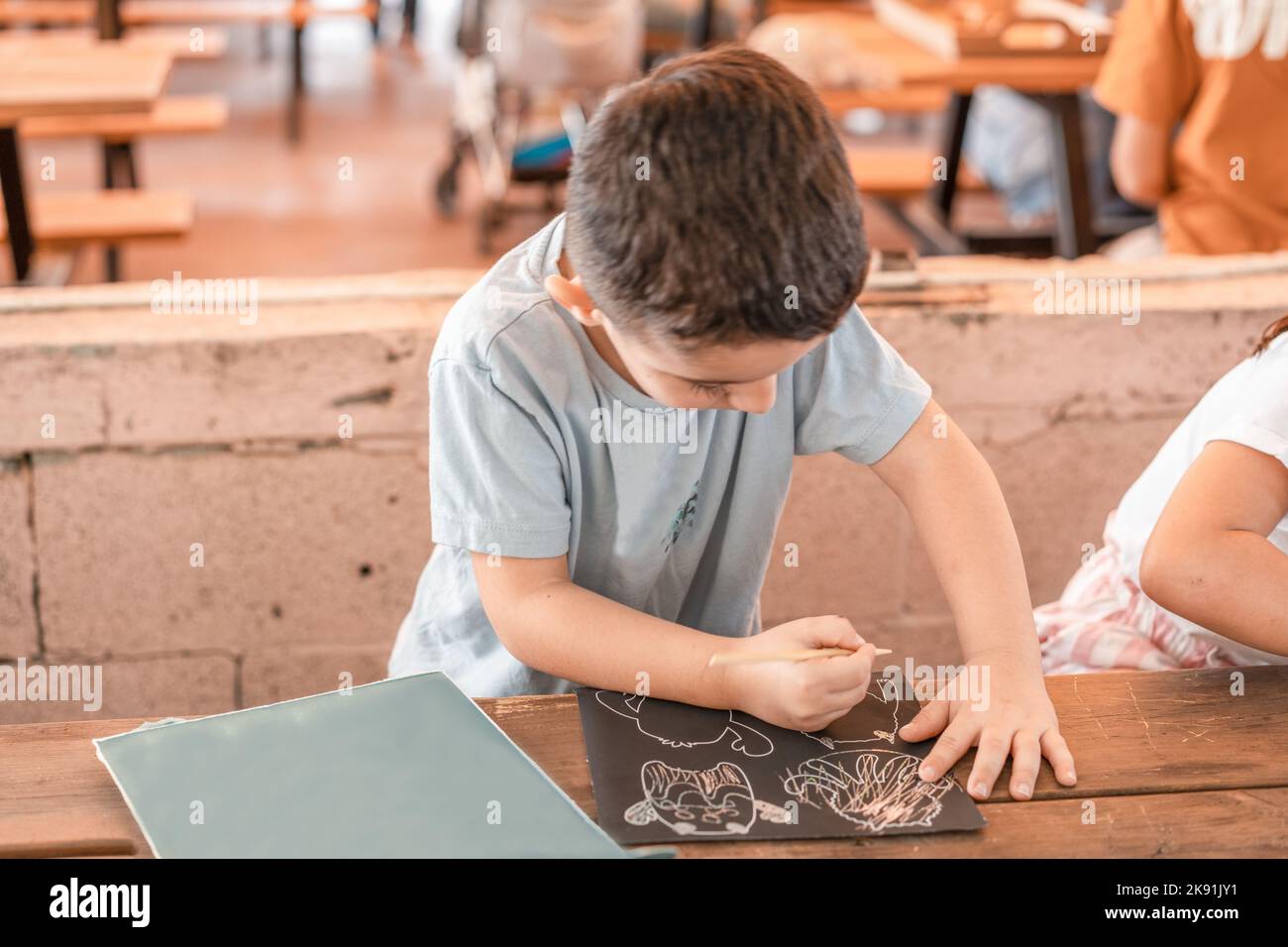Boy Draws Colored Scratches. Girl Using A Stick To Scratch In The Black Paper. Stock Photo