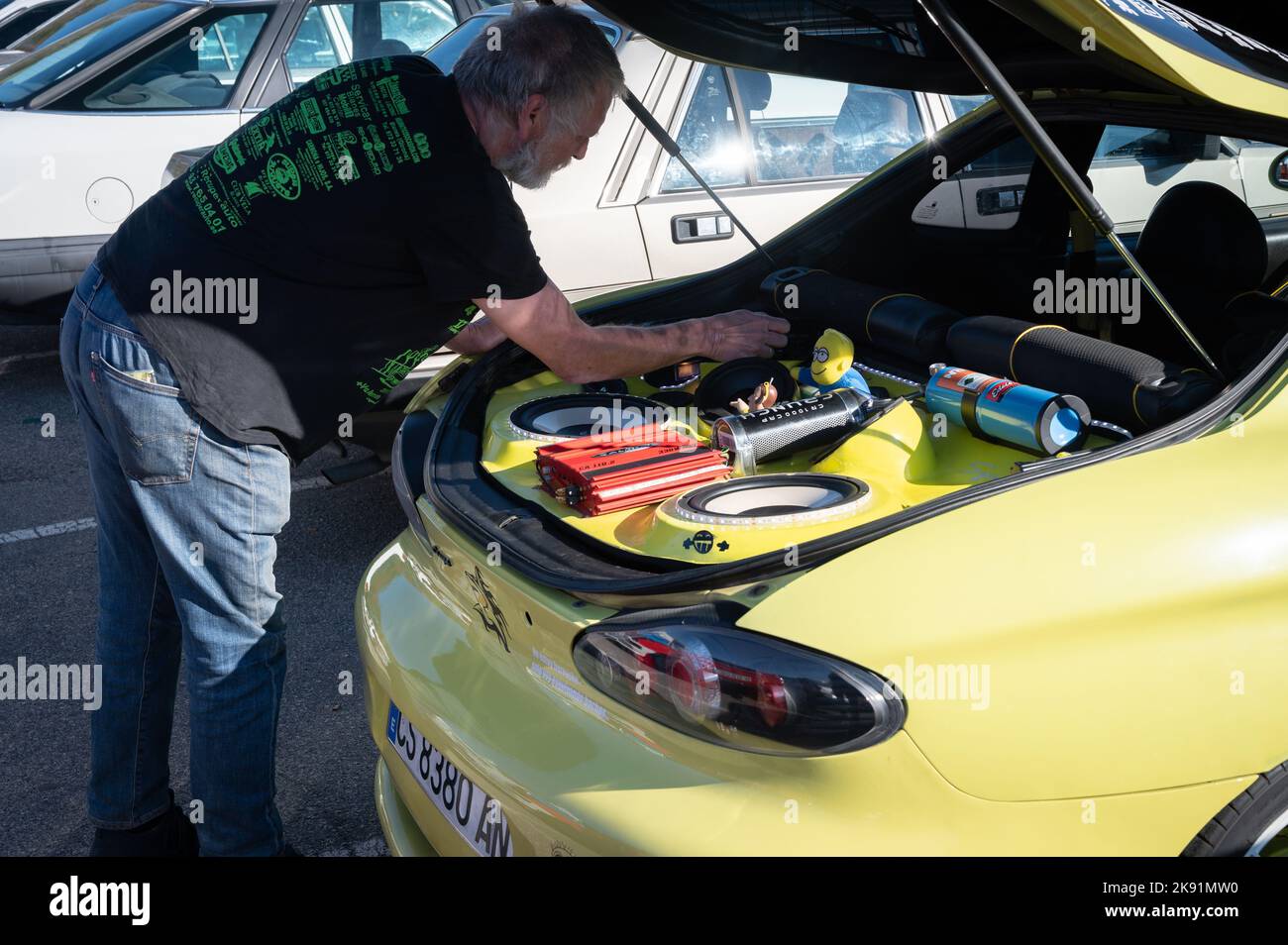 A man working on a tuned yellow Hyundai Coupe with stereo and toys in the trunk Stock Photo