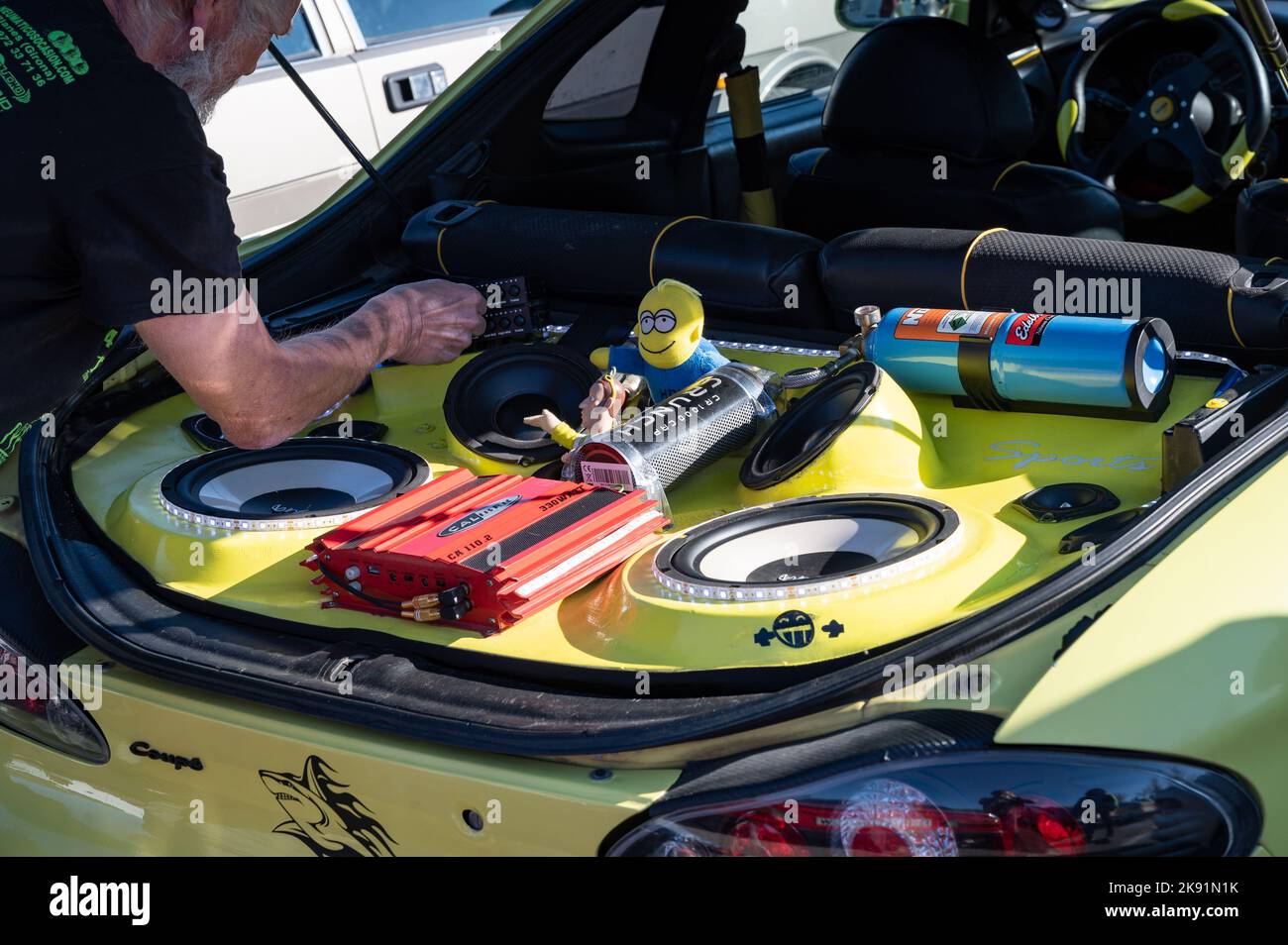 A man working on a tuned yellow Hyundai Coupe with stereo and toys in the trunk Stock Photo