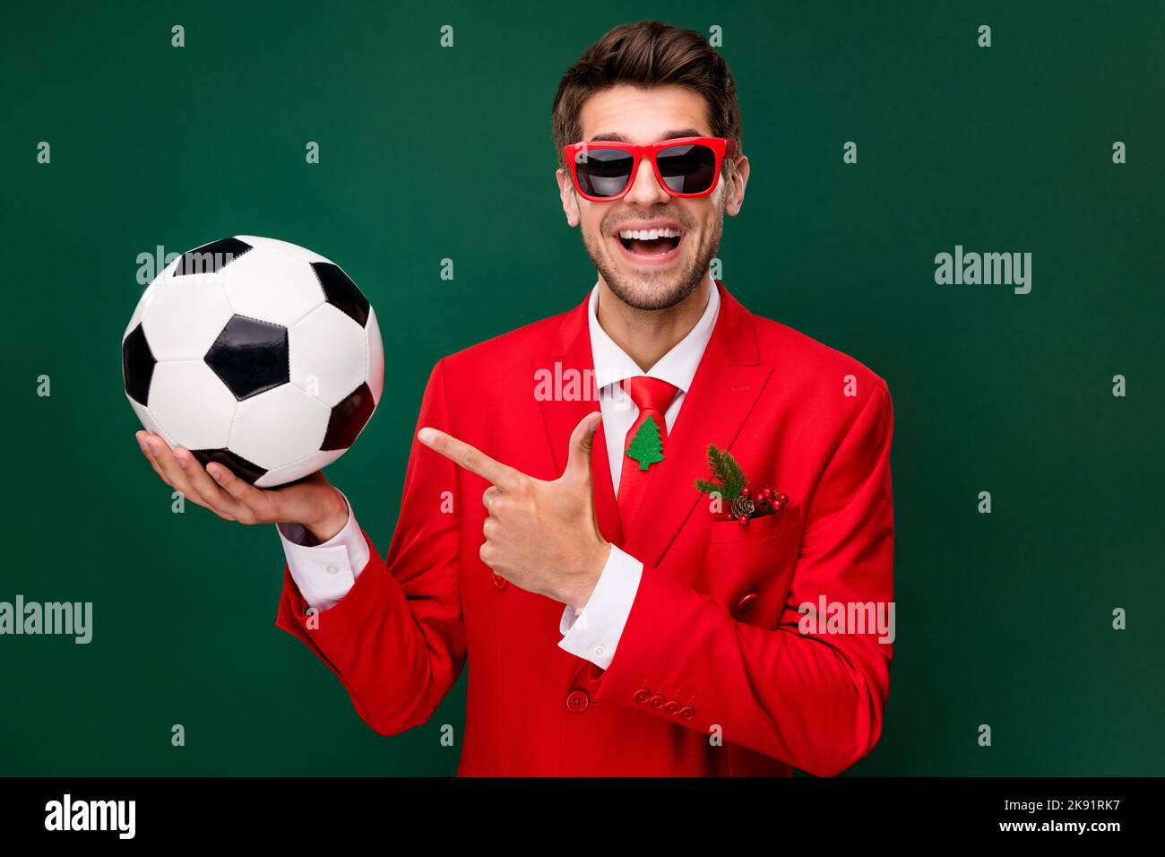 Portrait of handsome trendy cheerful guy wearing festal look demonstrating ball win match isolated over green color background Stock Photo