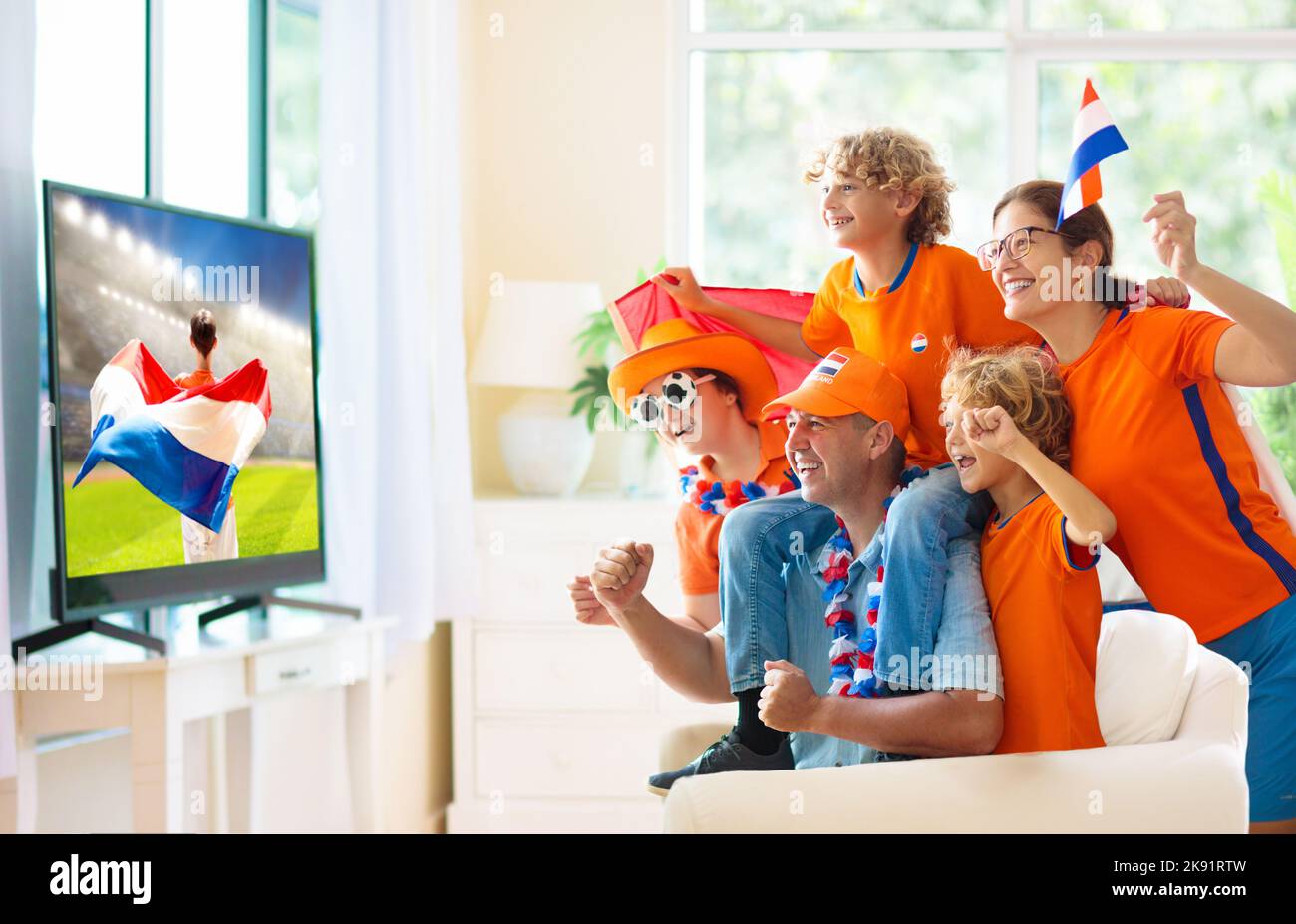 Group of Netherlands football fans watch tv at home. Go Holland. Friends watching Dutch soccer match in white living room. Stock Photo