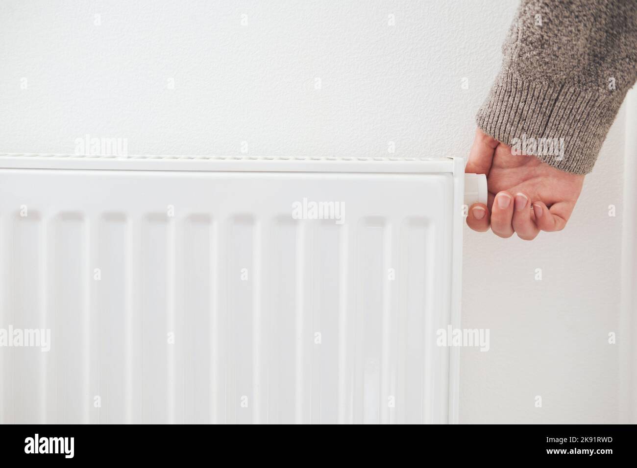 Hand turning down thermostat of a central heating radiator. Energy
