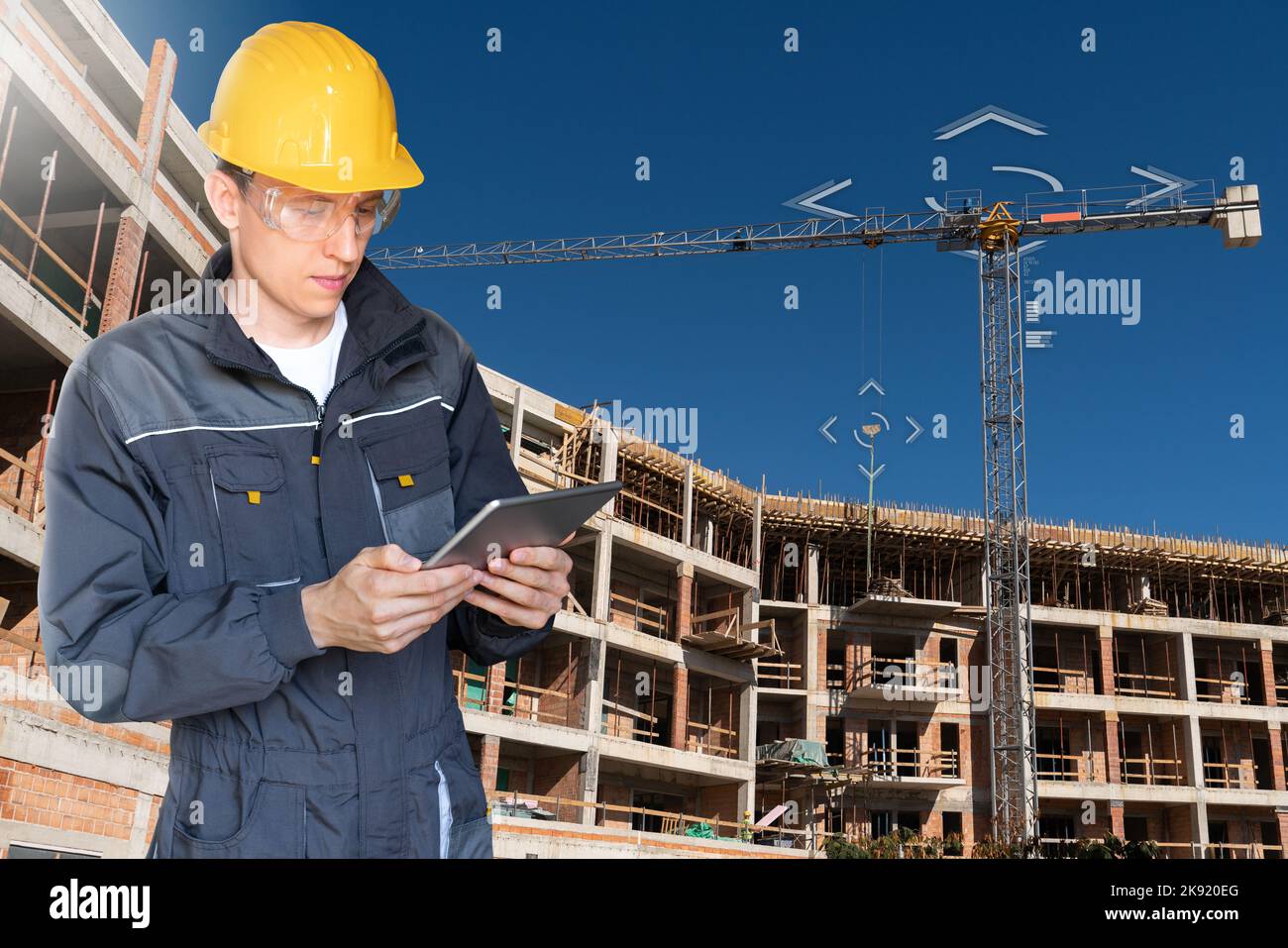 Builder with a digital tablet controls a remote-controlled unmanned crane. Digital transformation in construction industry.  Stock Photo