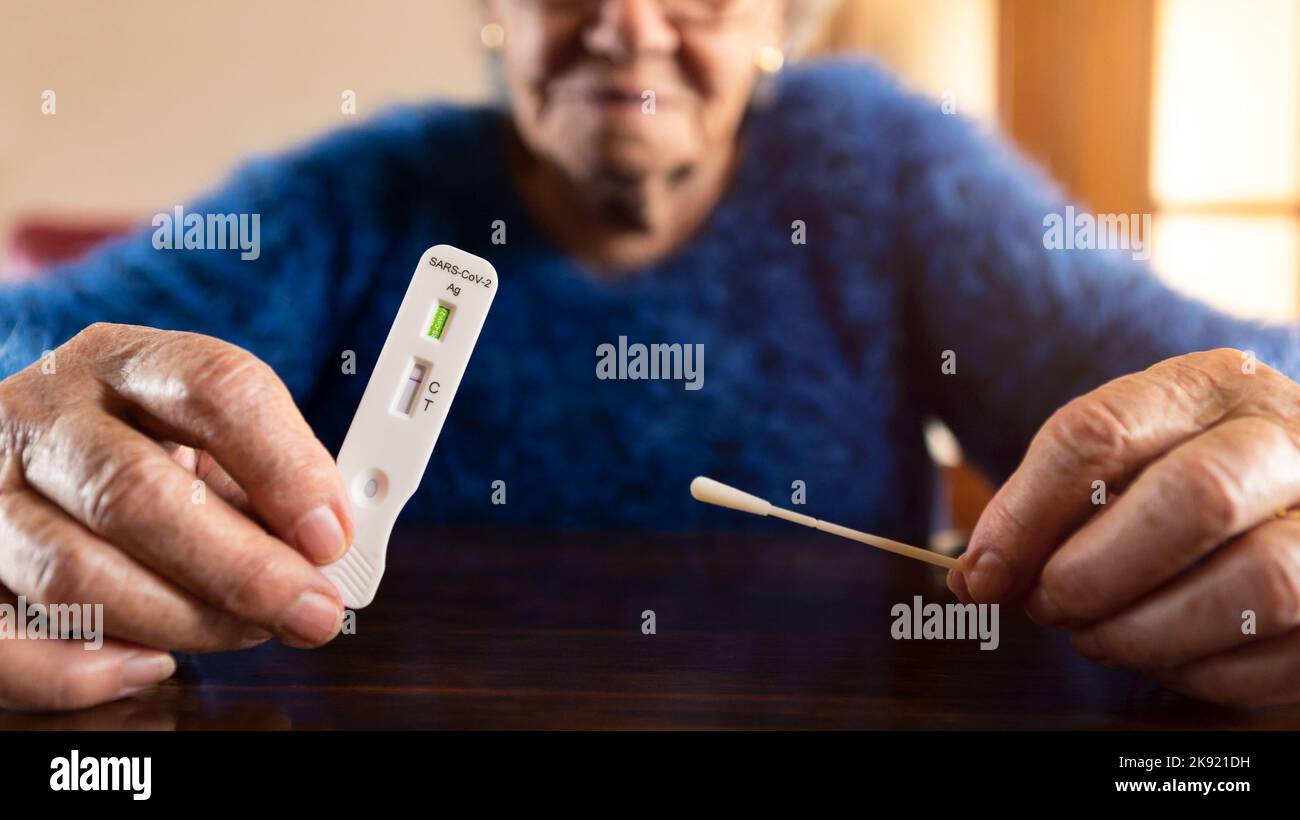 Close-up of caucasian grandma hand holding a buffer dropper for seft detection of coronavirus at home. Grandmother using antigen cassette of pcr expre Stock Photo